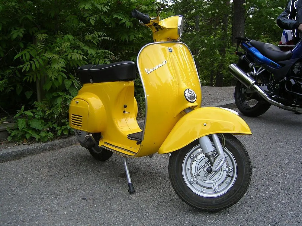 A yellow Vespa scooter parked on its stand by the roadside